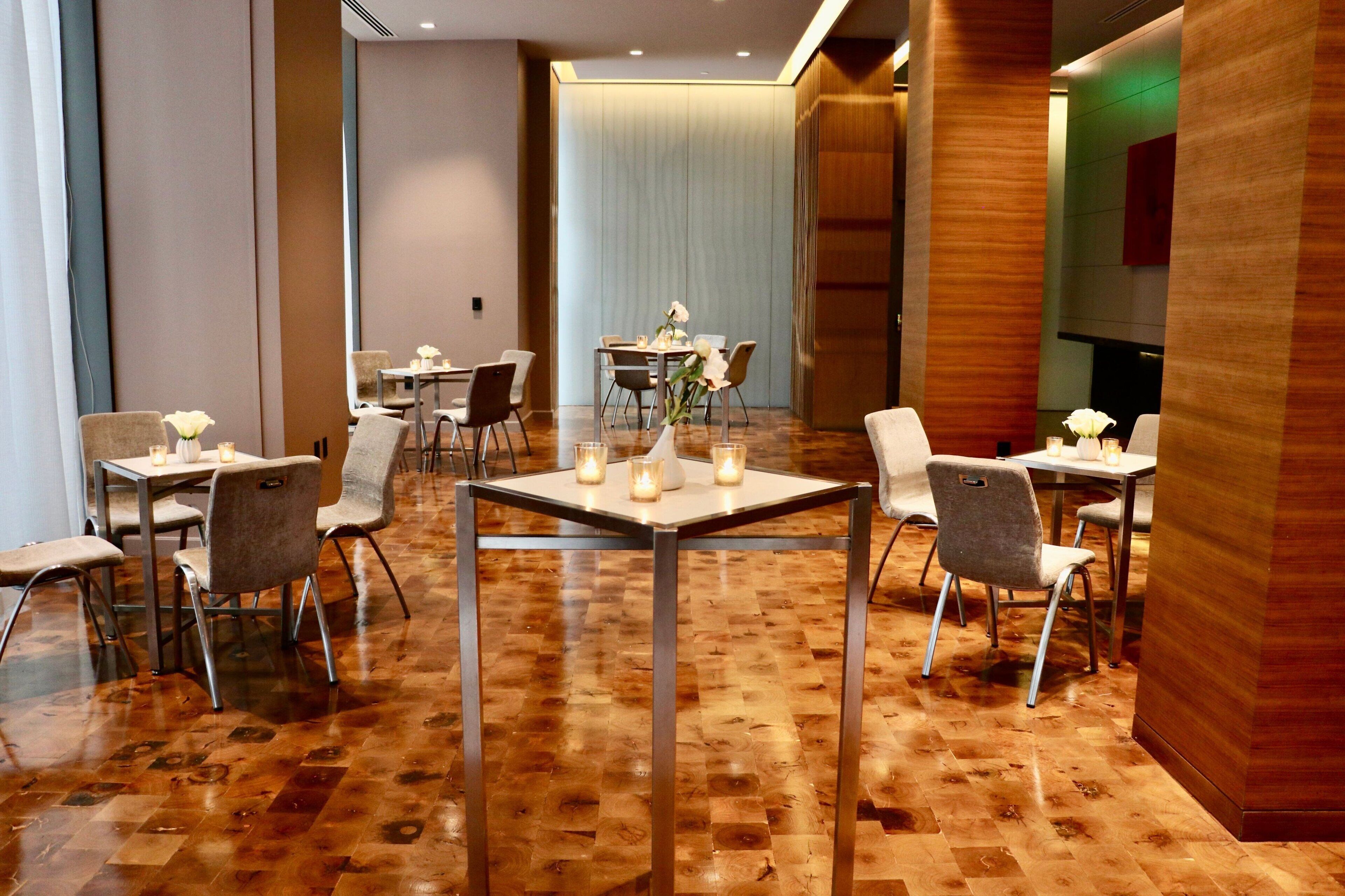 A hotel dining area with multiple tables and chairs, wooden flooring, and a modern interior design.