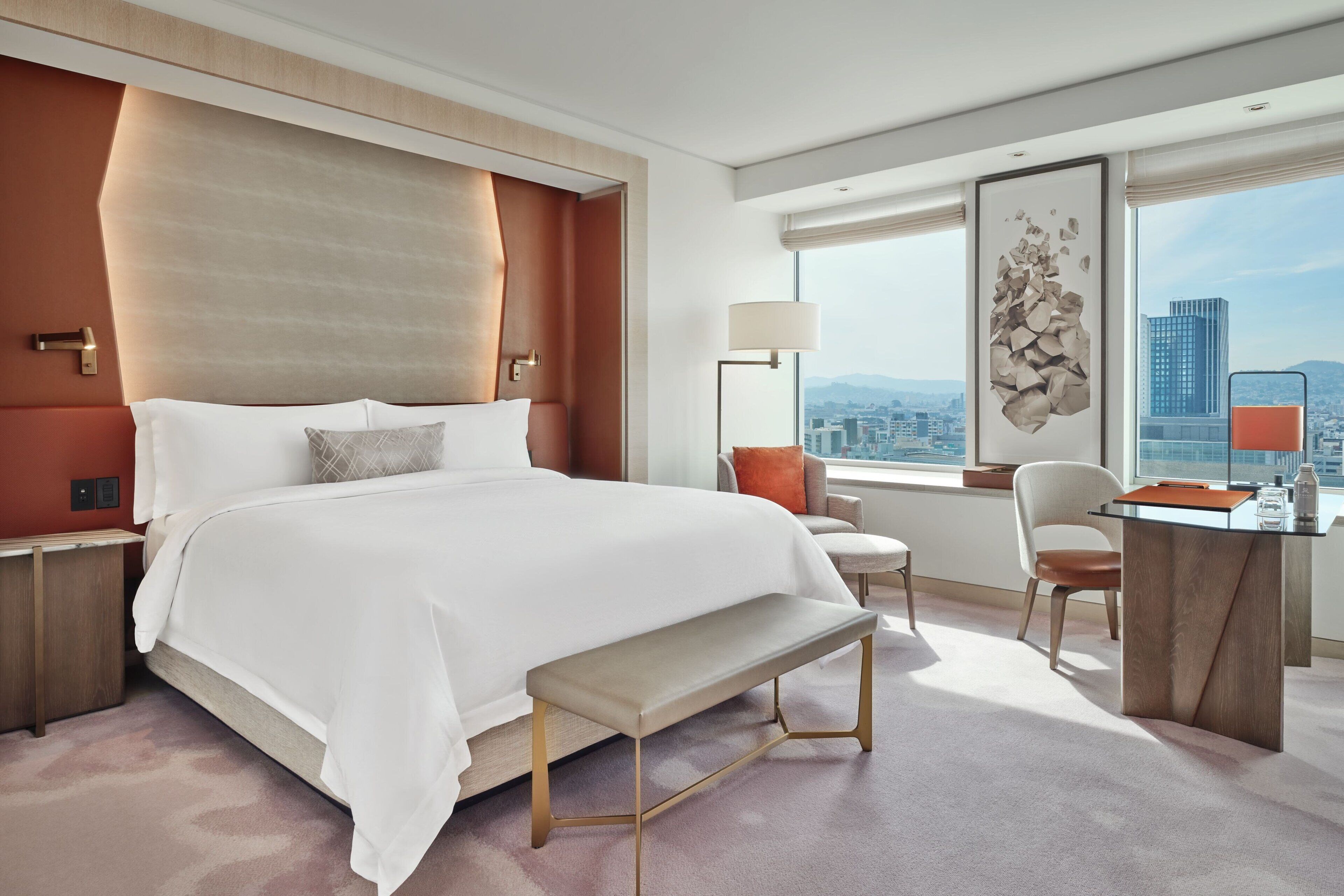 A modern hotel room with a large bed, a desk, and a view of the city.