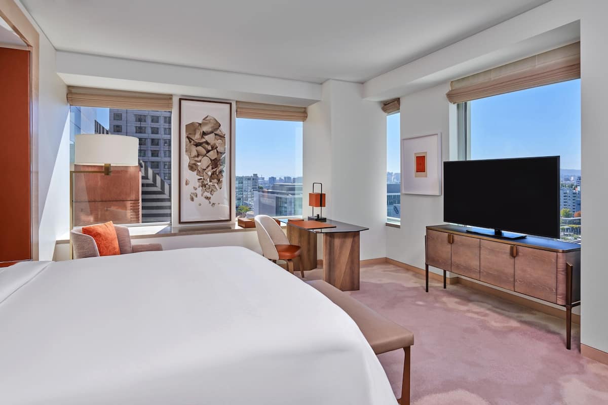 A modern hotel room with a large bed, a desk, a television, and a city view.
