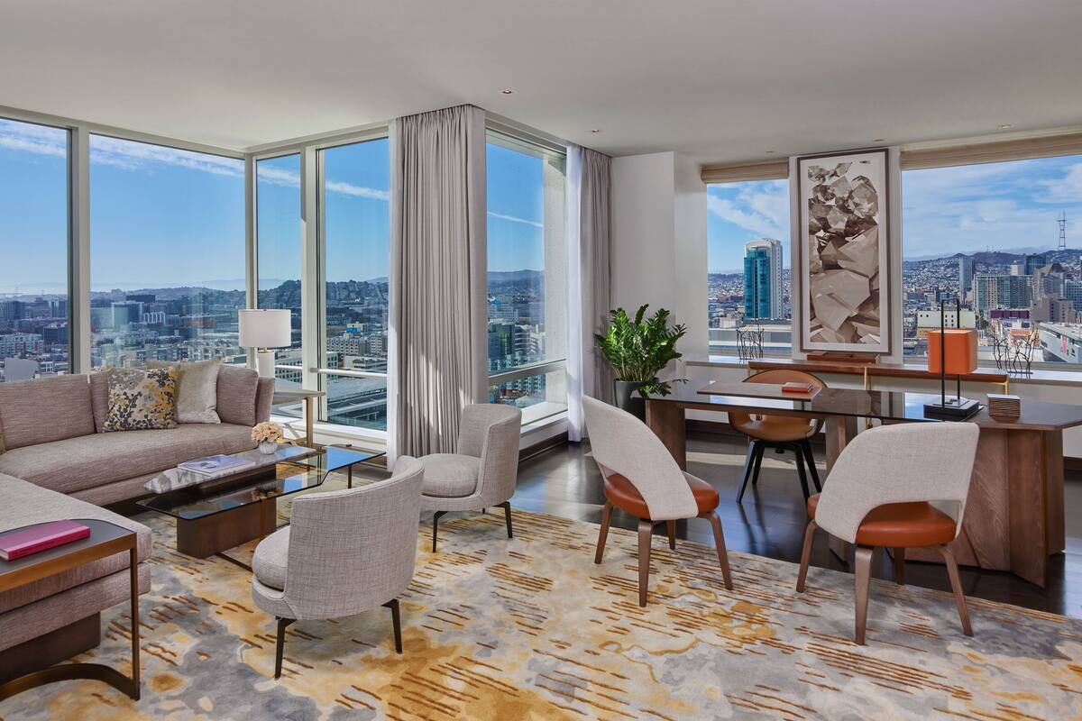 A modern living room with a city view, a sofa, chairs, a coffee table, and a desk with a lamp.
