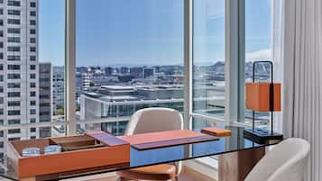 Un espace de bureau moderne avec un bureau en verre, un fauteuil en cuir et une vue sur la ville grâce à de grandes fenêtres.
