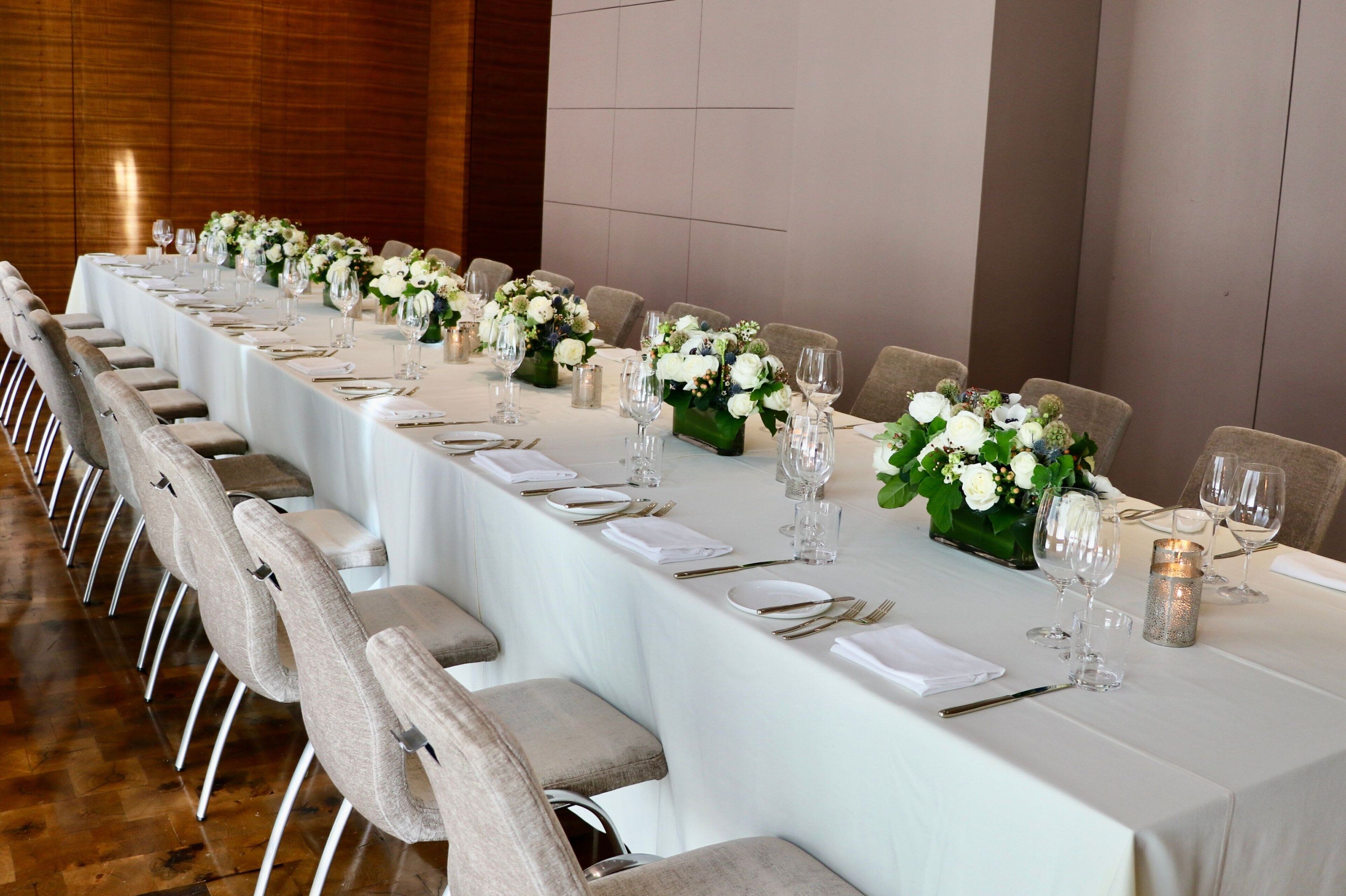 A long dining table set with white tablecloths, chairs, and floral centerpieces.