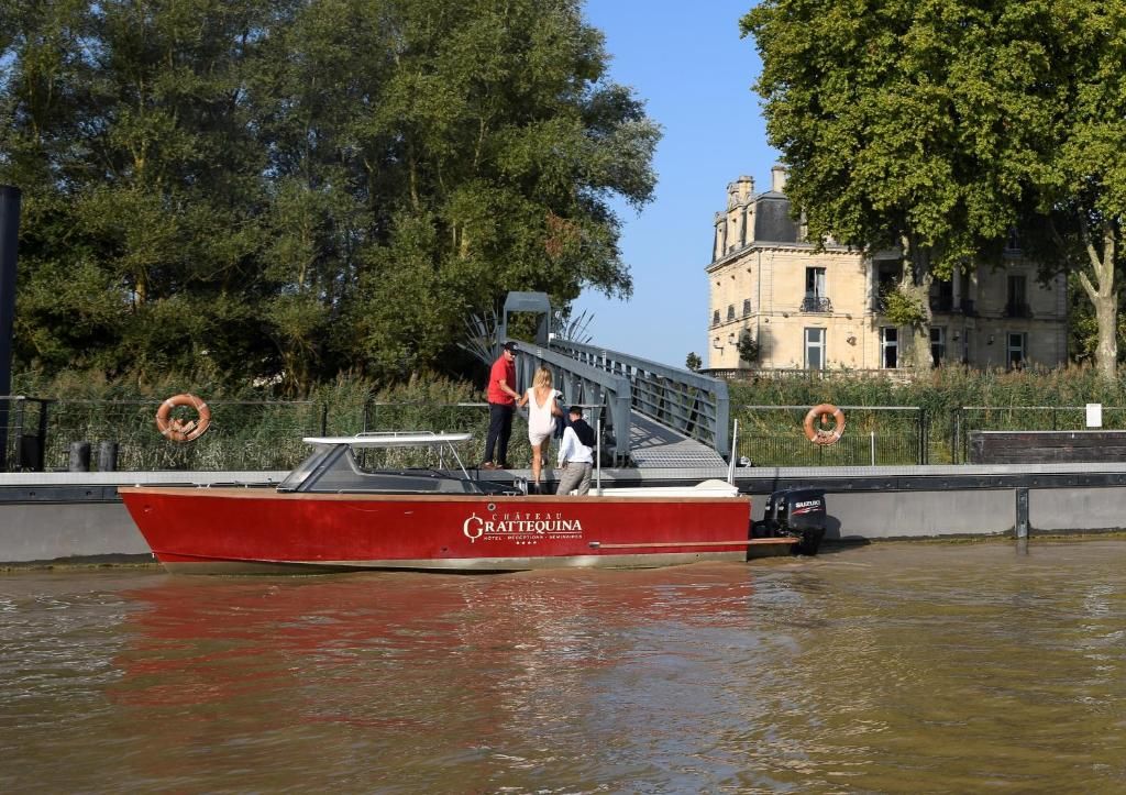 A red boat with 'Chateau Grattequin' written on it, docked at a pier with a building in the background.