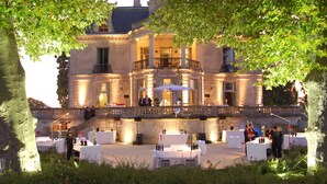 An outdoor event with tables and chairs set up in front of a historic building with a balcony. - Chateau Grattequina (Blanquefort)