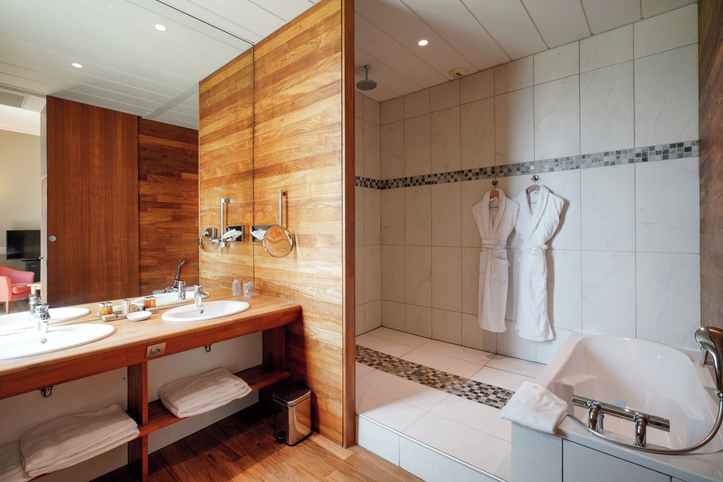 A modern bathroom with a wooden vanity, dual sinks, a large mirror, a shower with a glass door, and a bathtub.