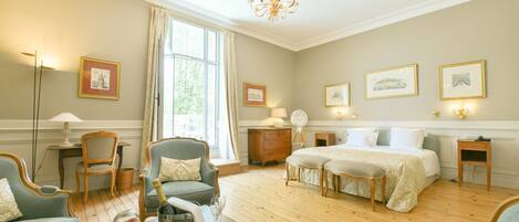 A spacious bedroom with a large bed, two bedside tables, a wooden dresser, and a sitting area with a chair and a small table.