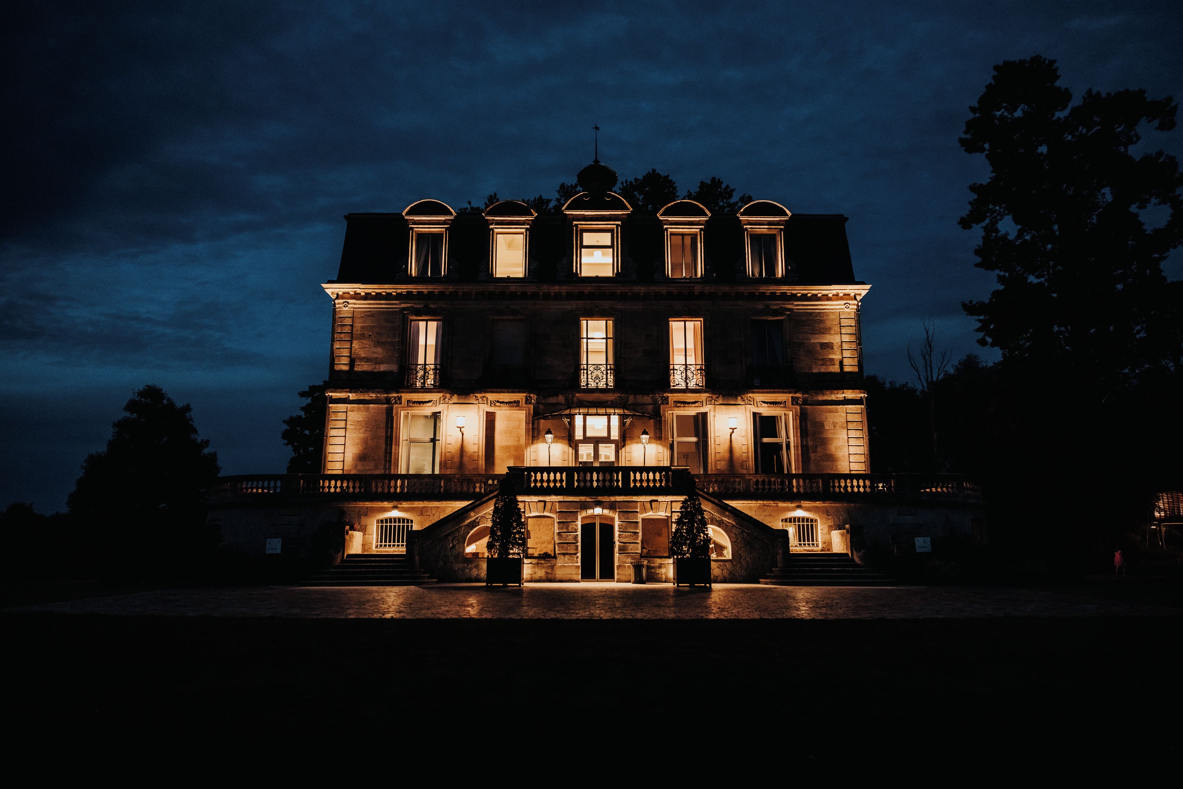 A large, multi-story building with a symmetrical facade, illuminated windows, and a central entrance with steps.
