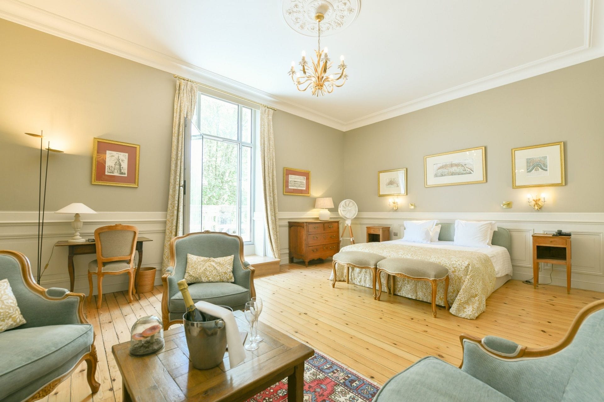 A well-lit bedroom with a large bed, two bedside tables, a nightstand, a chair, a desk, and a chandelier.