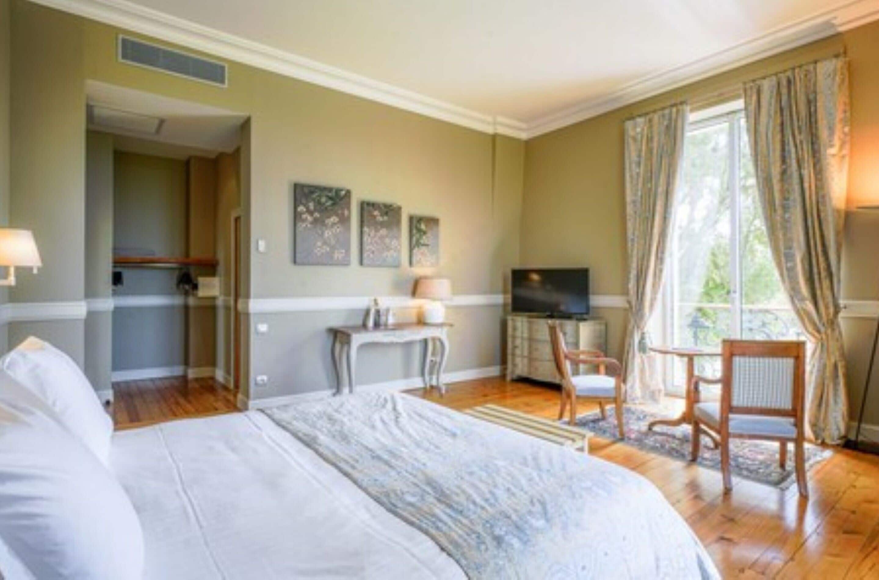 A hotel room with a bed, a desk, a television, and a window with curtains.
