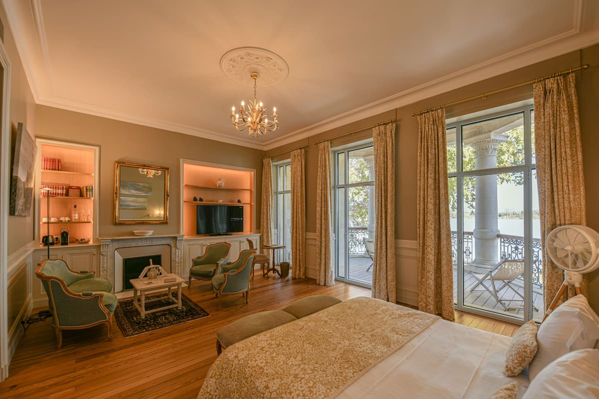 A spacious bedroom with a large bed, a fireplace, and a balcony with outdoor seating.