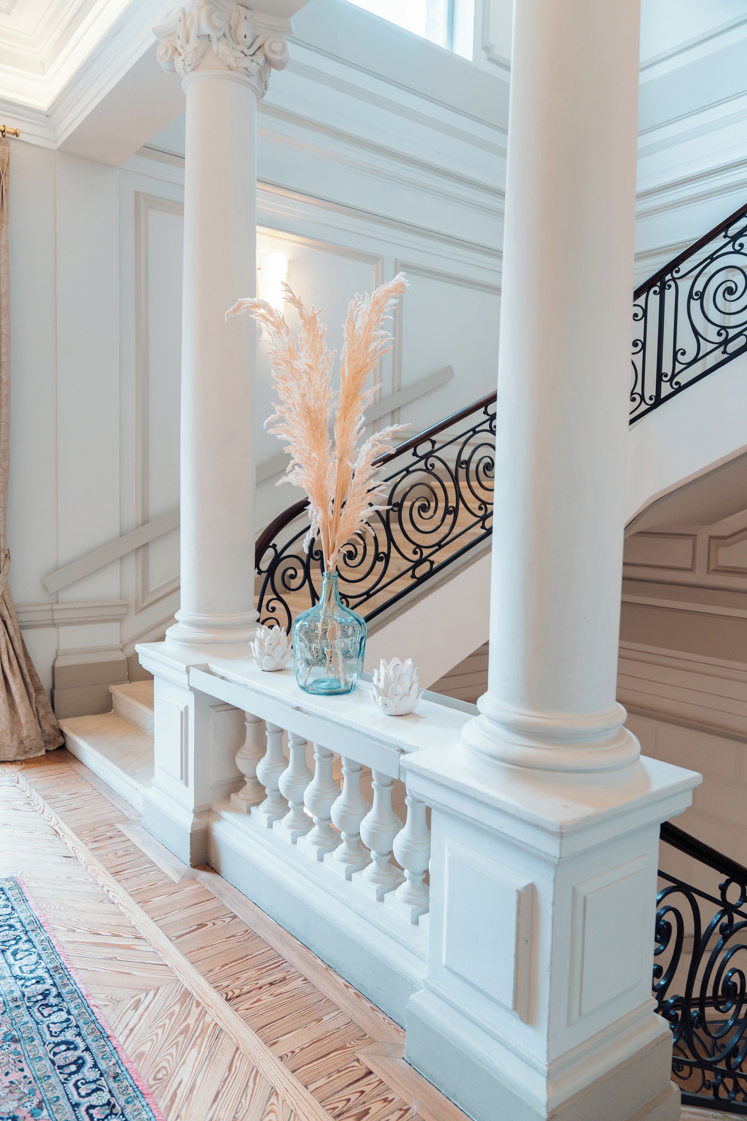 Un magnifique escalier avec des colonnes blanches et une rampe en fer forgé noir.