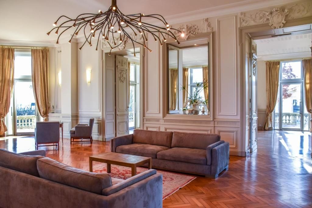 Un salón comedor amplio con una lámpara moderna, sofás cómodos y un espejo grande que refleja el ambiente.