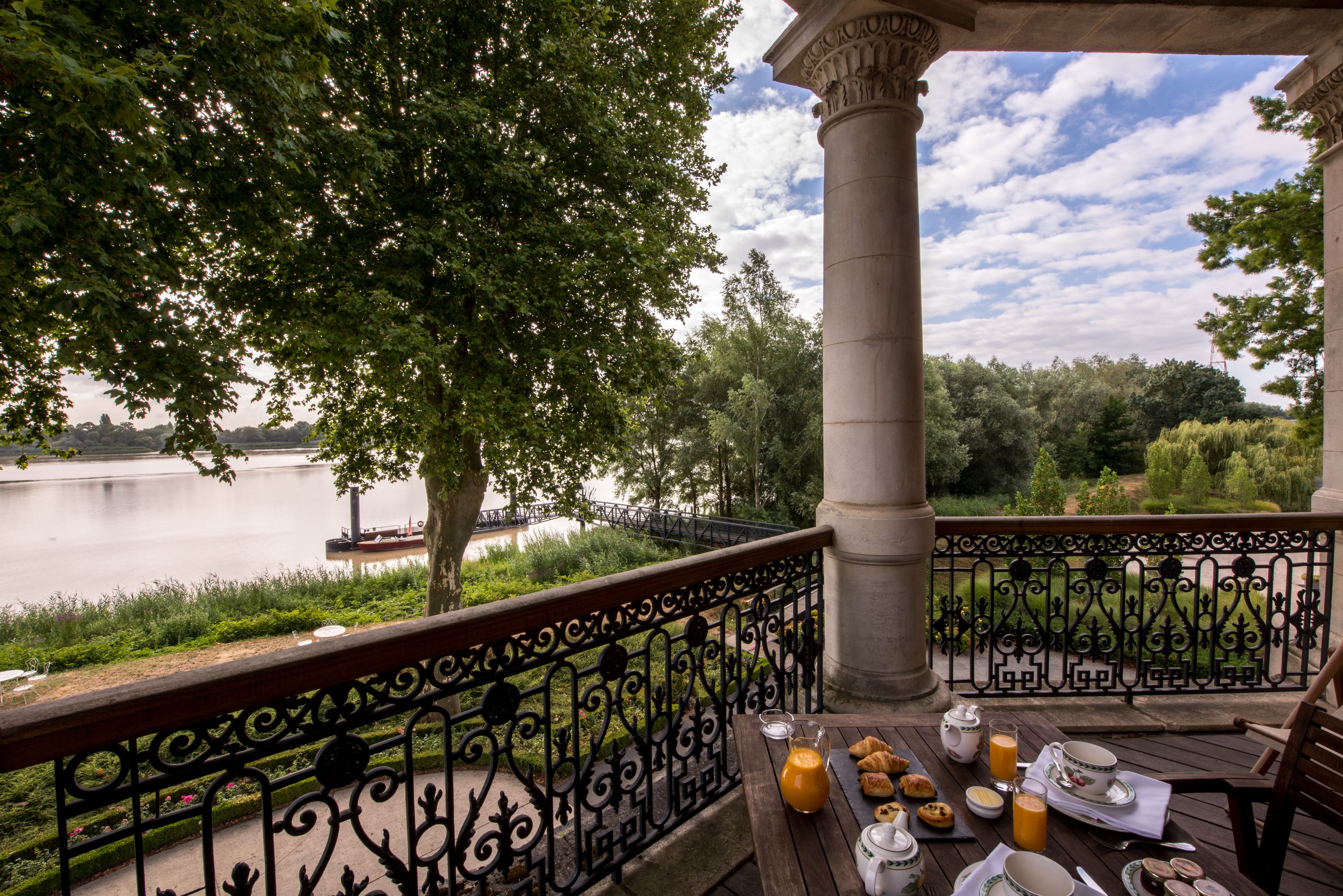 Una terraza con vista al río, una mesa lista para el desayuno y una barandilla decorativa.