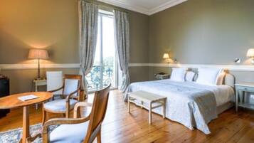 A hotel room with a bed, bedside tables, a desk with a chair, and a window with curtains.