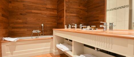A bathroom with wooden panel walls, a wooden vanity with a mirror, a bathtub, and shelves with towels.