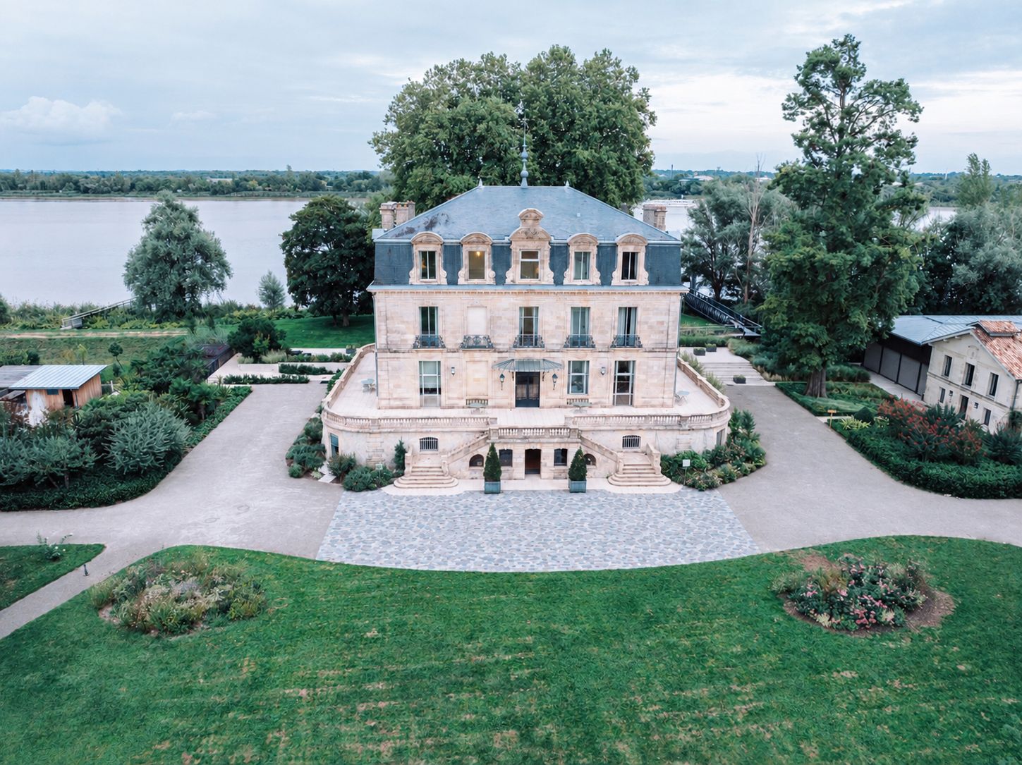 Un grand immeuble à étages, doté d’une façade symétrique, d’une entrée centrale avec des marches et d’un jardin paysager qui l’entoure.