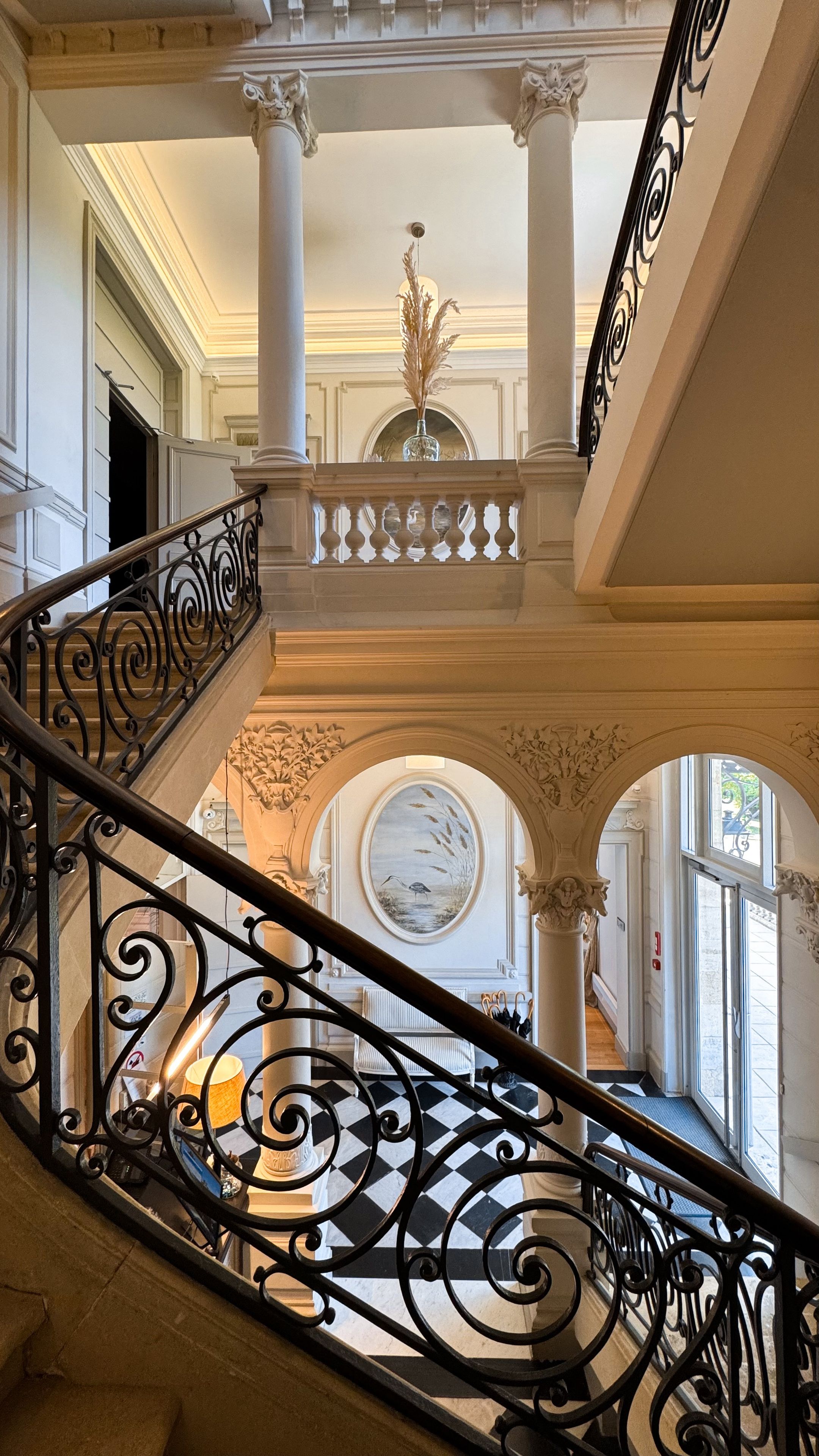 A grand staircase with ornate black railings, white columns, and a decorative vase at the top.