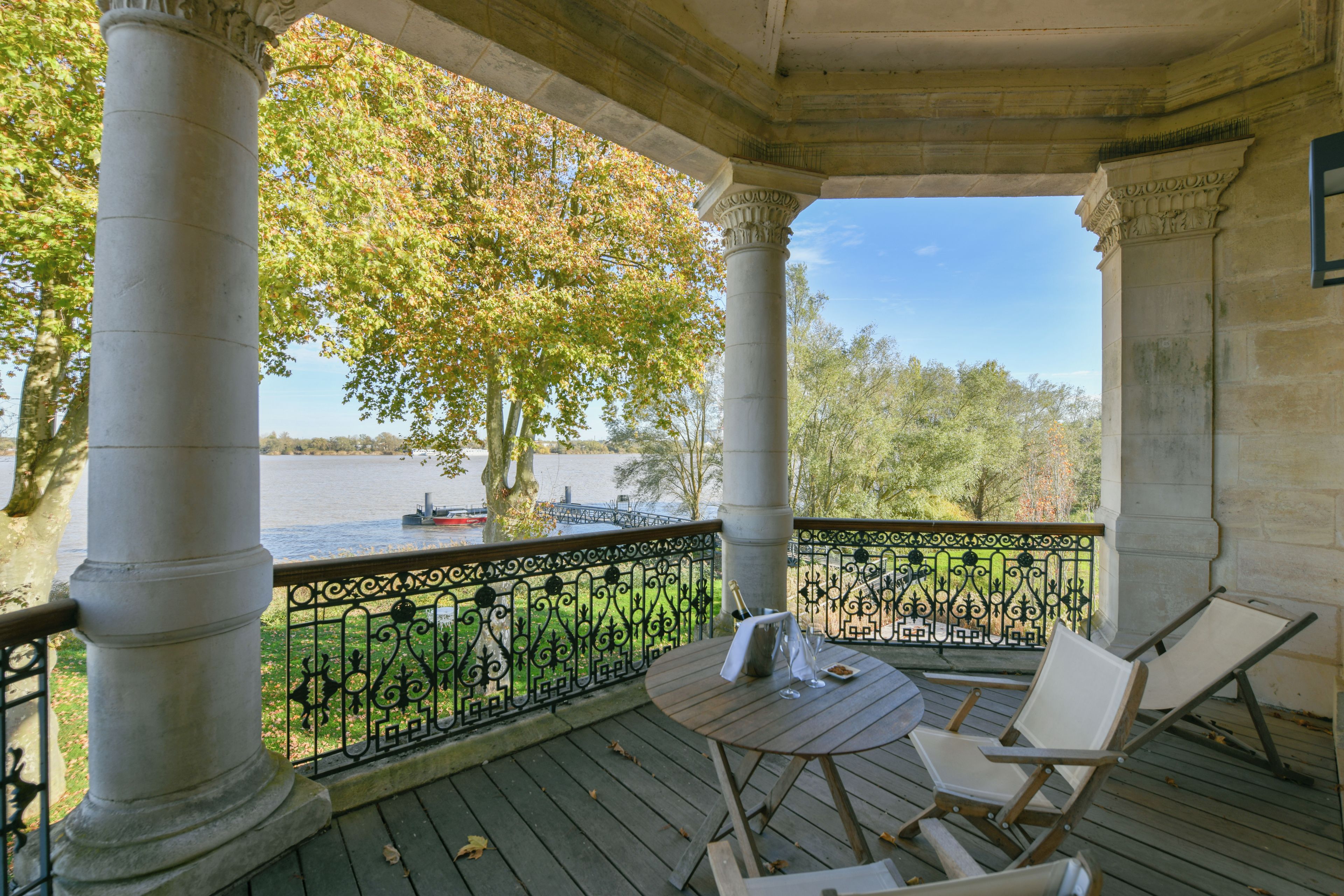 A covered outdoor area with a table and chairs, overlooking a body of water with boats.
