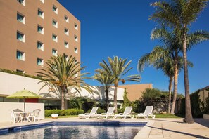 A pool area with lounge chairs and a table, surrounded by palm trees and a building with multiple windows. - Fiesta Inn Tijuana Otay (Tijuana)