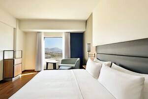 Habitación de hotel con una cama grande, un escritorio, una silla y vistas a las montañas.