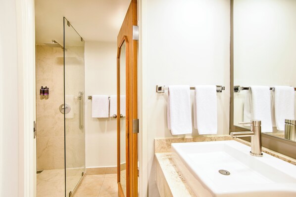 Uma casa de banho moderna com chuveiro envidraçado, lavatório com espelho e várias toalhas brancas.