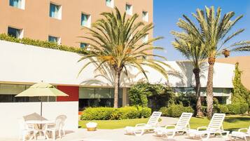 A hotel pool area with a clear blue sky, palm trees, and a building with multiple windows.
