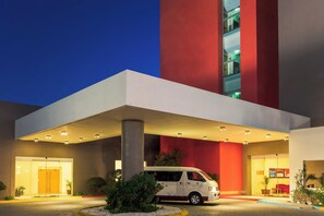 A modern building with a white and red facade, a covered entrance, and a van parked outside. - Fiesta Inn Tijuana Otay (Tijuana)