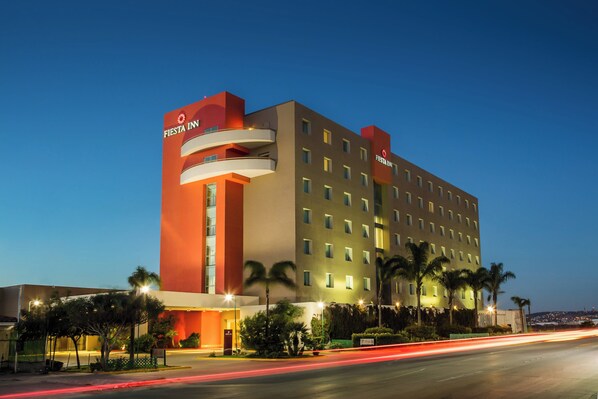 A multi-story hotel with a prominent red and beige facade, multiple balconies, and a well-lit entrance. - Fiesta Inn Tijuana Otay (Tijuana)