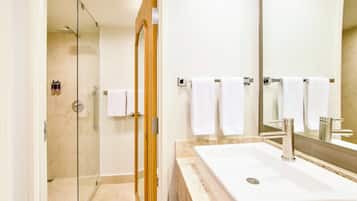 Un baño moderno con ducha de vidrio, un lavamanos grande con espejo y varias toallas blancas.