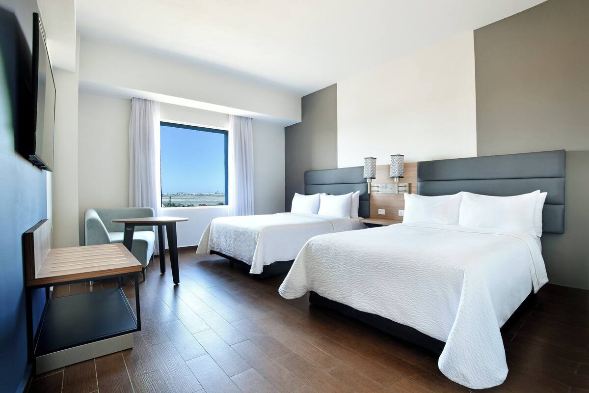 Une chambre d’hôtel avec deux lits, un bureau, une chaise et une grande fenêtre donnant sur la ville.