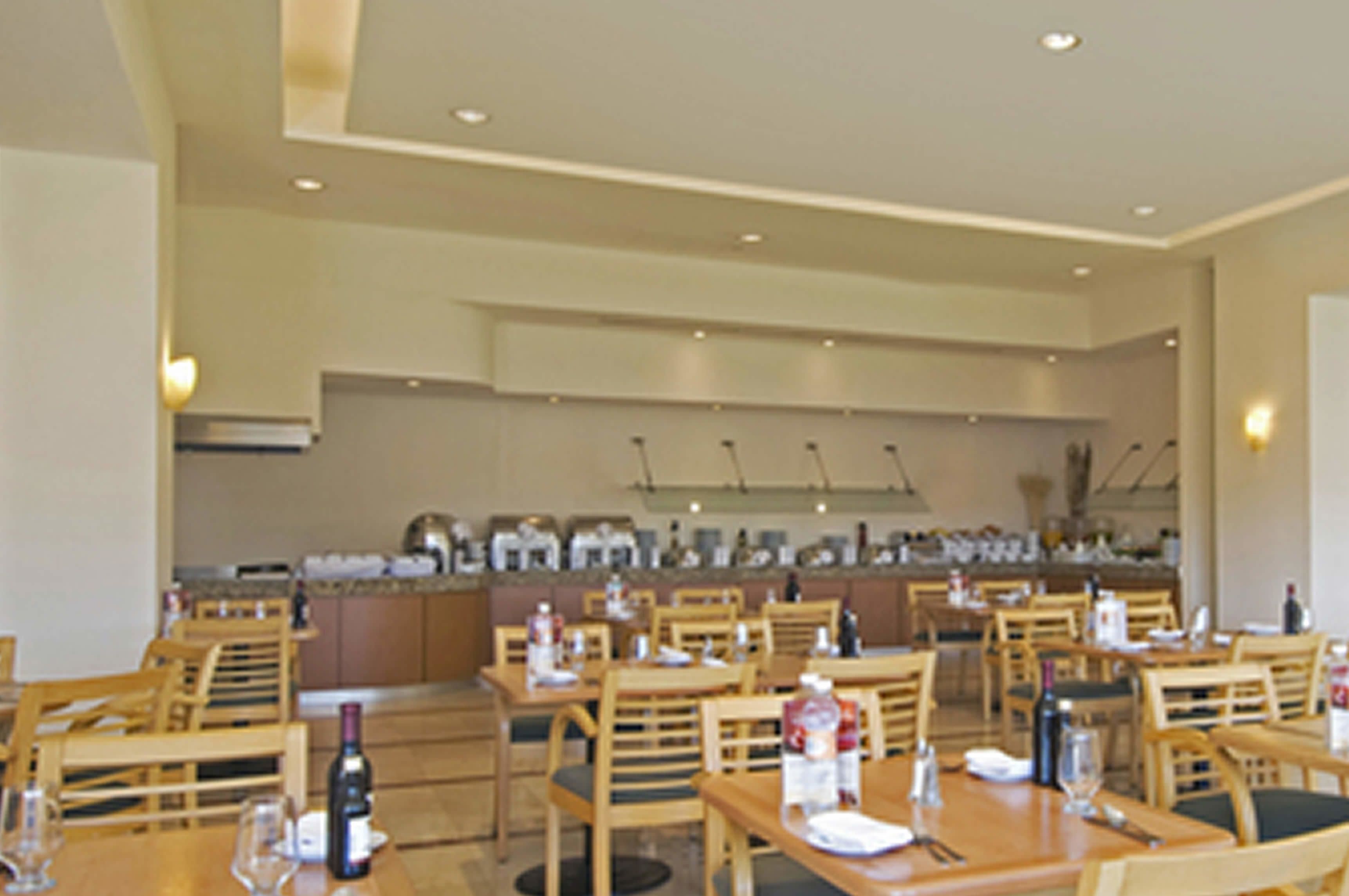 A restaurant with wooden tables and chairs, a bar area, and a kitchen in the background.