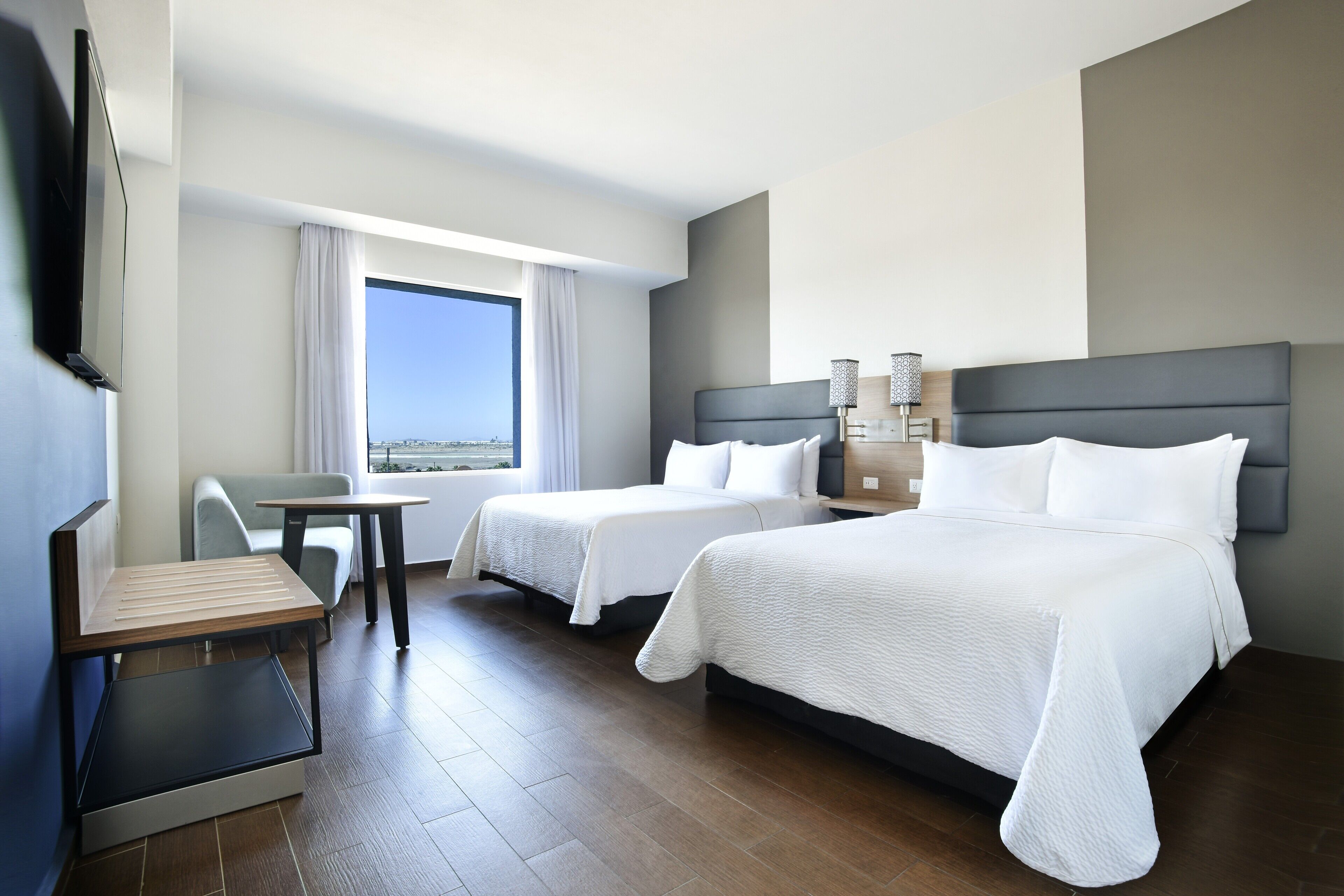 A hotel room with two beds, a desk, a TV, and a window with a view.