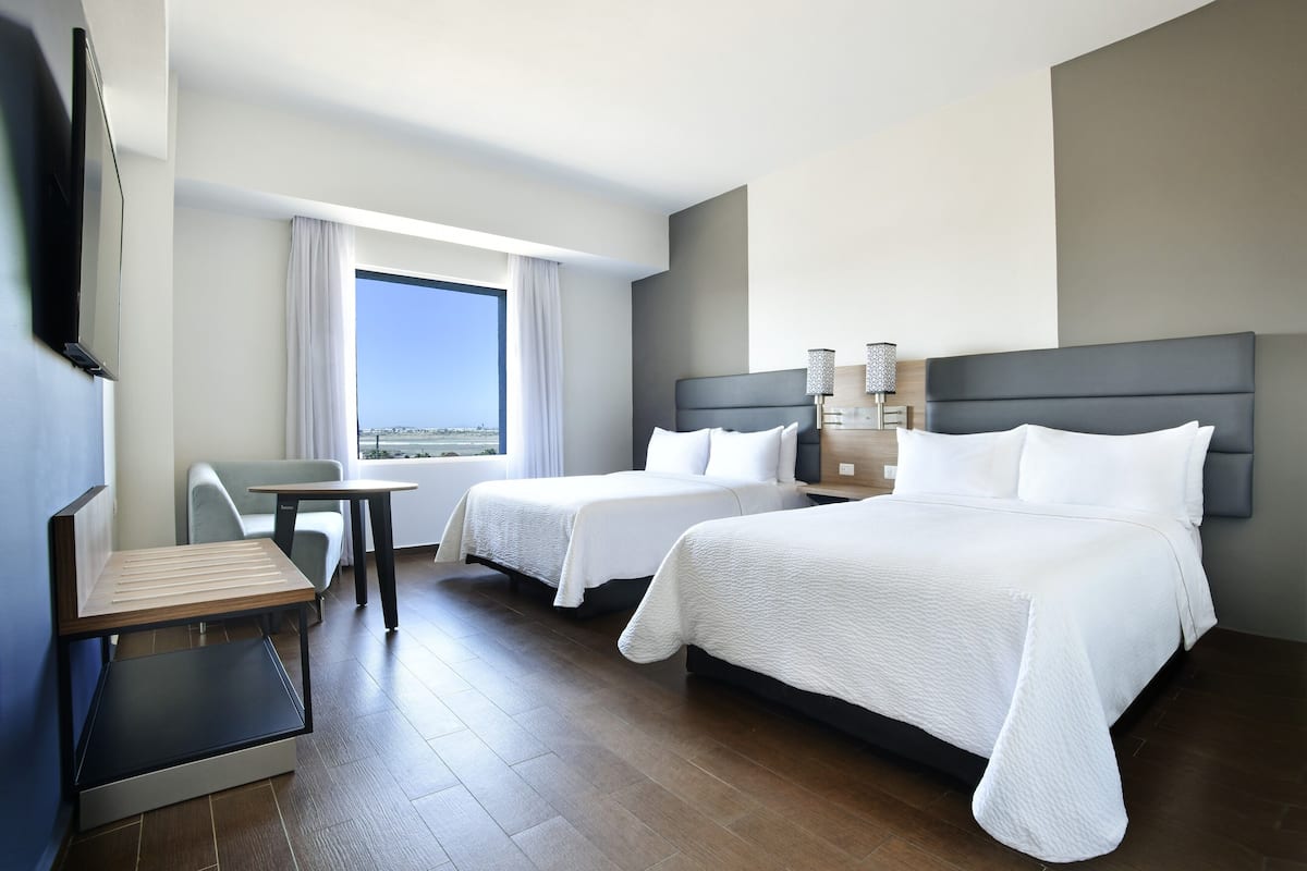 Une chambre d’hôtel avec deux lits, un bureau, une télévision et une fenêtre donnant sur un paysage agréable.