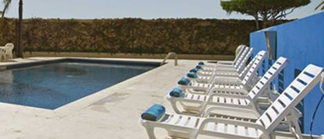 Una piscina con sillones de descanso alineados a lo largo de su borde.