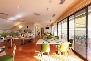 A spacious dining area with multiple tables and chairs, a kitchen in the background, and large windows providing natural light. - Hotel Excelsior Magenta (Magenta)