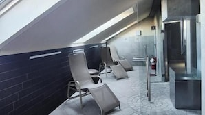 A modern waiting area with a sloped ceiling, lounge chairs, a glass partition, and a visible fire extinguisher. - Hotel Excelsior Magenta (Magenta)