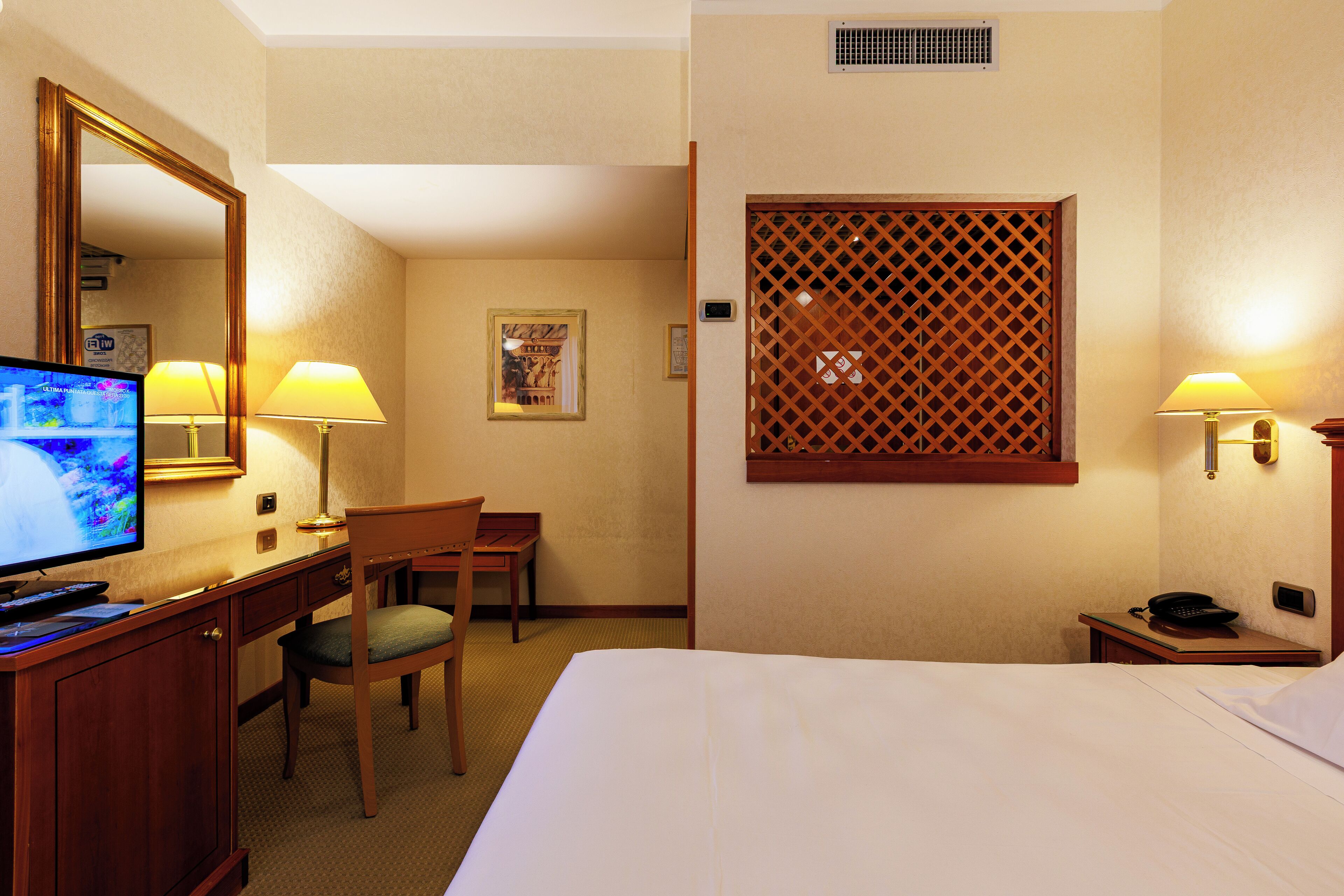 Une chambre d’hôtel équipée d’un lit, d’un bureau, d’une chaise, d’une télévision, de lampes et d’un paravent décoratif.