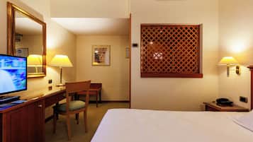 Une chambre d’hôtel équipée d’un lit, d’un bureau, d’une chaise, d’une télévision, de lampes et d’un paravent décoratif.