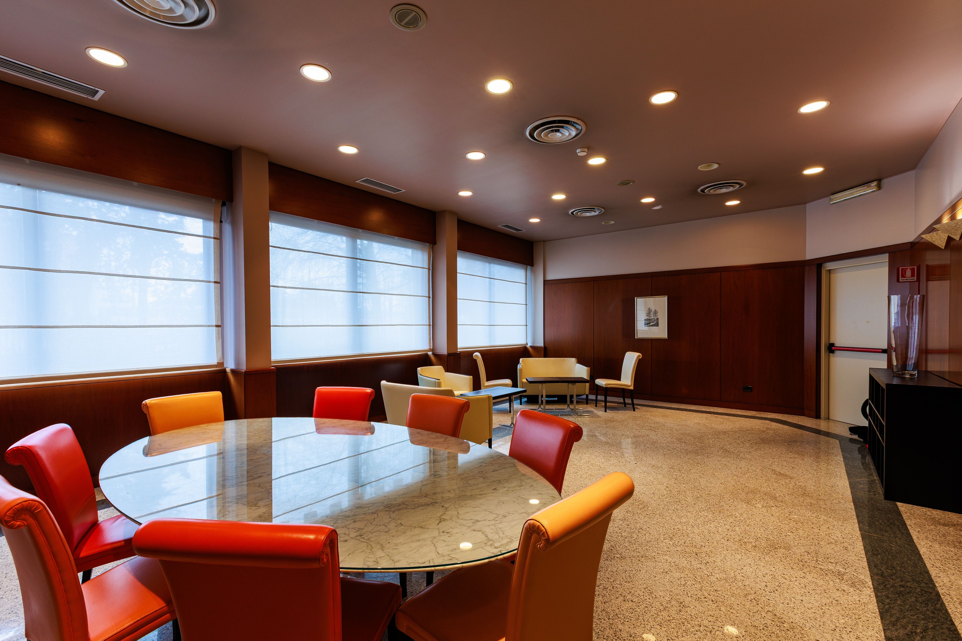 A conference room with a round table and chairs, large windows, and a fire extinguisher on the wall.