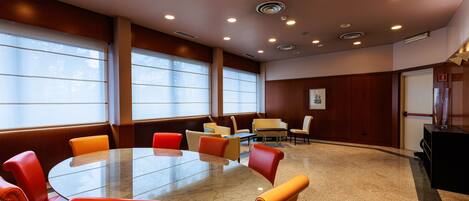 A conference room with a round table and chairs, large windows, and a fire extinguisher on the wall.
