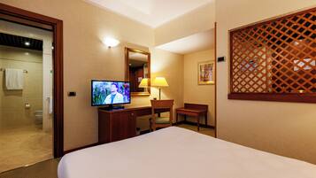 A hotel room with a bed, a desk, a television, a chair, a lamp, and a bathroom visible through an open door.