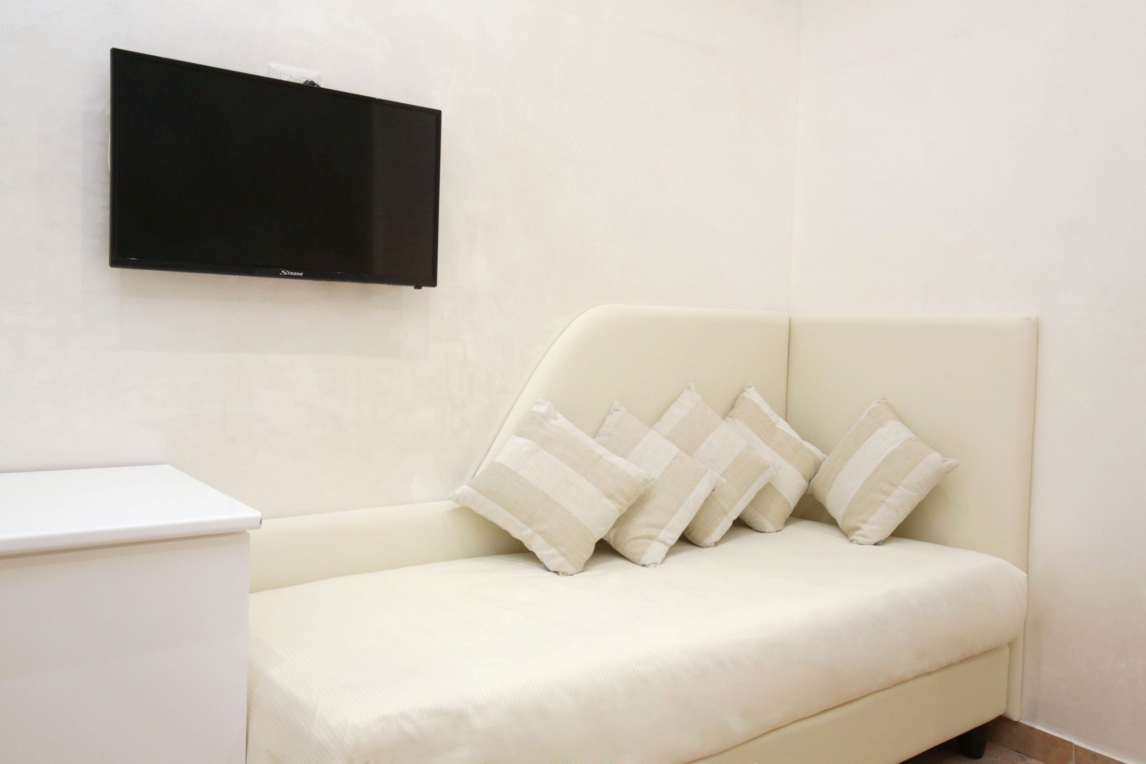 A modern room with a white sofa, a flat-screen TV mounted on the wall, and a small white table.
