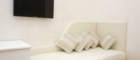 A modern room with a white sofa, a flat-screen TV mounted on the wall, and a small white table.