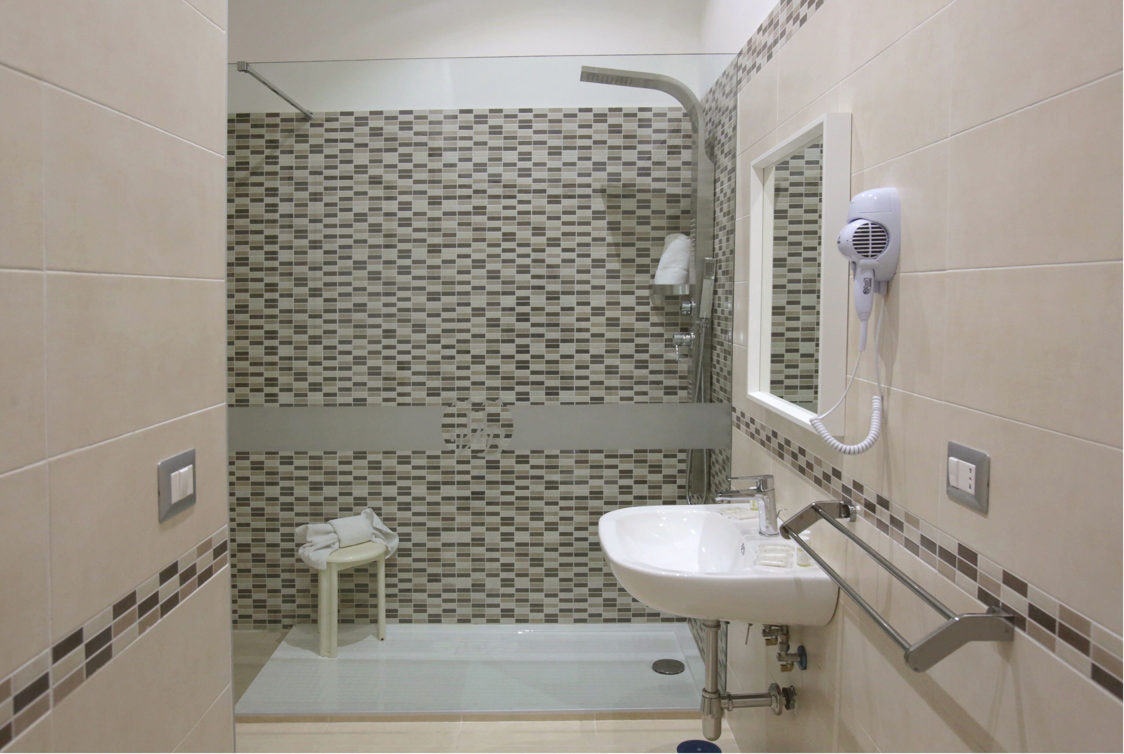 A bathroom with a tiled shower wall, a sink with a towel rack, and a hairdryer mounted on the wall.