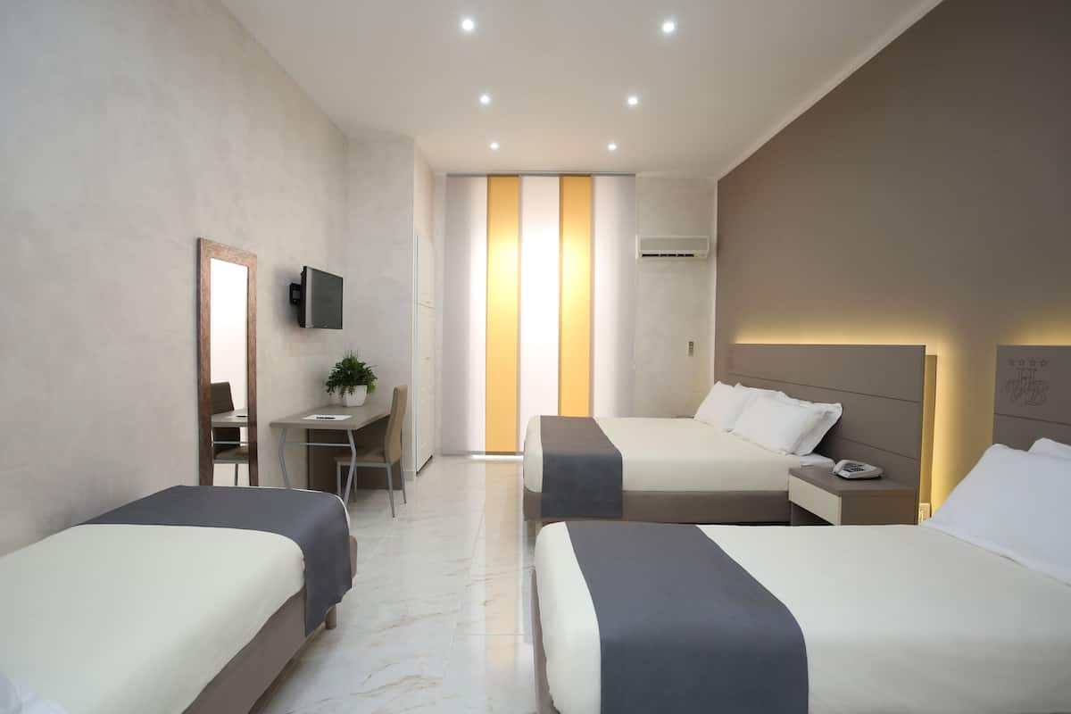 A hotel room with two beds, a desk, a chair, a TV, and an air conditioning unit.
