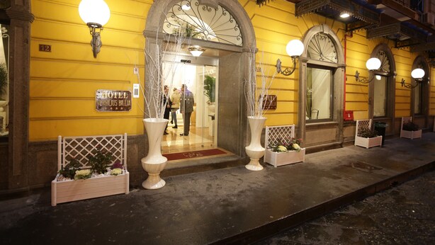 A hotel entrance with a yellow facade, large arched doorways, and white planters with flowers. - Hotel Vergilius Billia (Naples)