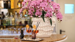 A bar area with a large white pot of pink orchids, two glasses with orange slices, and a bottle of liquor on a marble countertop. - Hotel Vergilius Billia (Naples)