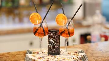 Three glasses of orange-colored beverage with straws, a decorative candle, and a tray with confetti on a marble surface.