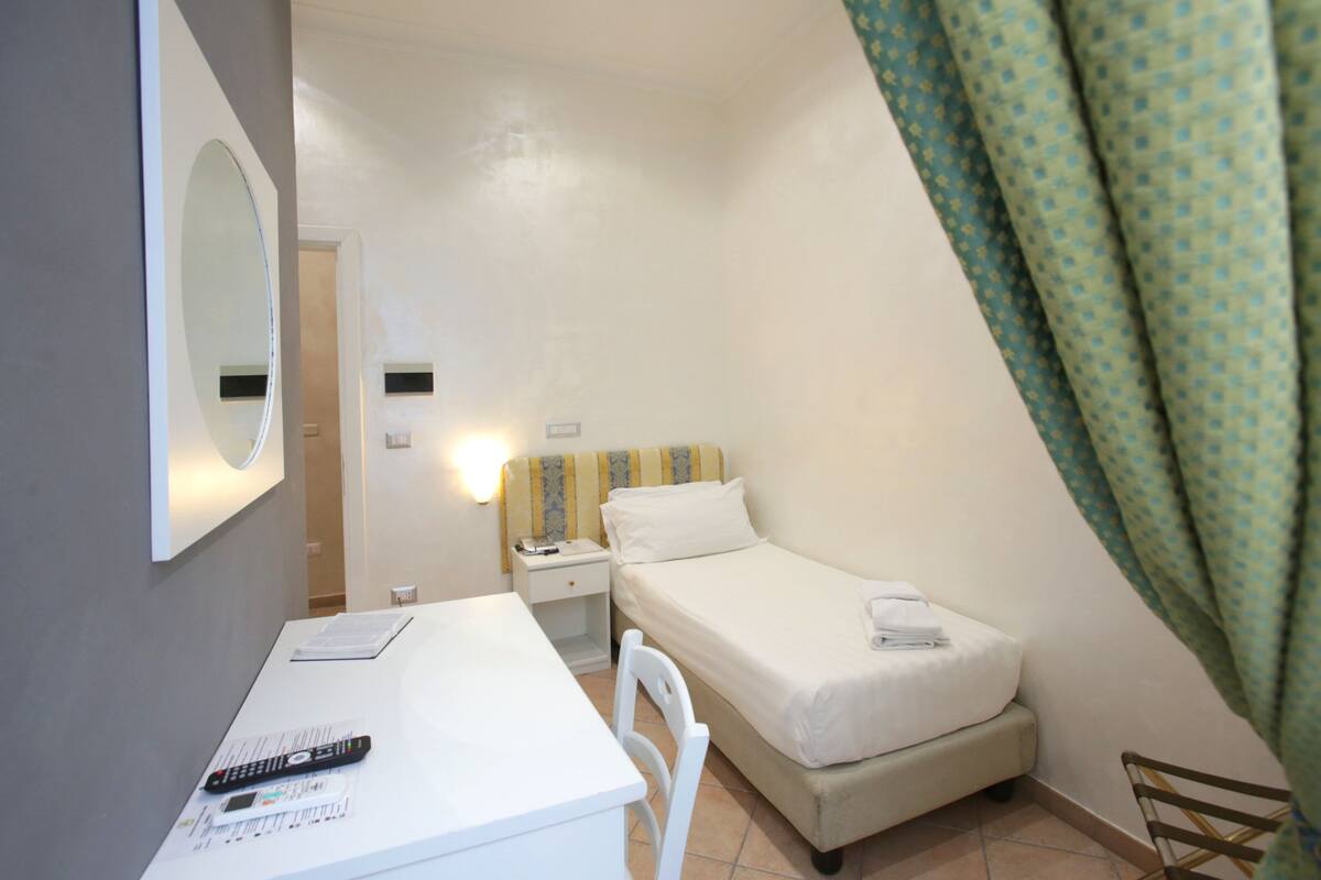 A small, single-bed room with a desk, chair, and a mirror.
