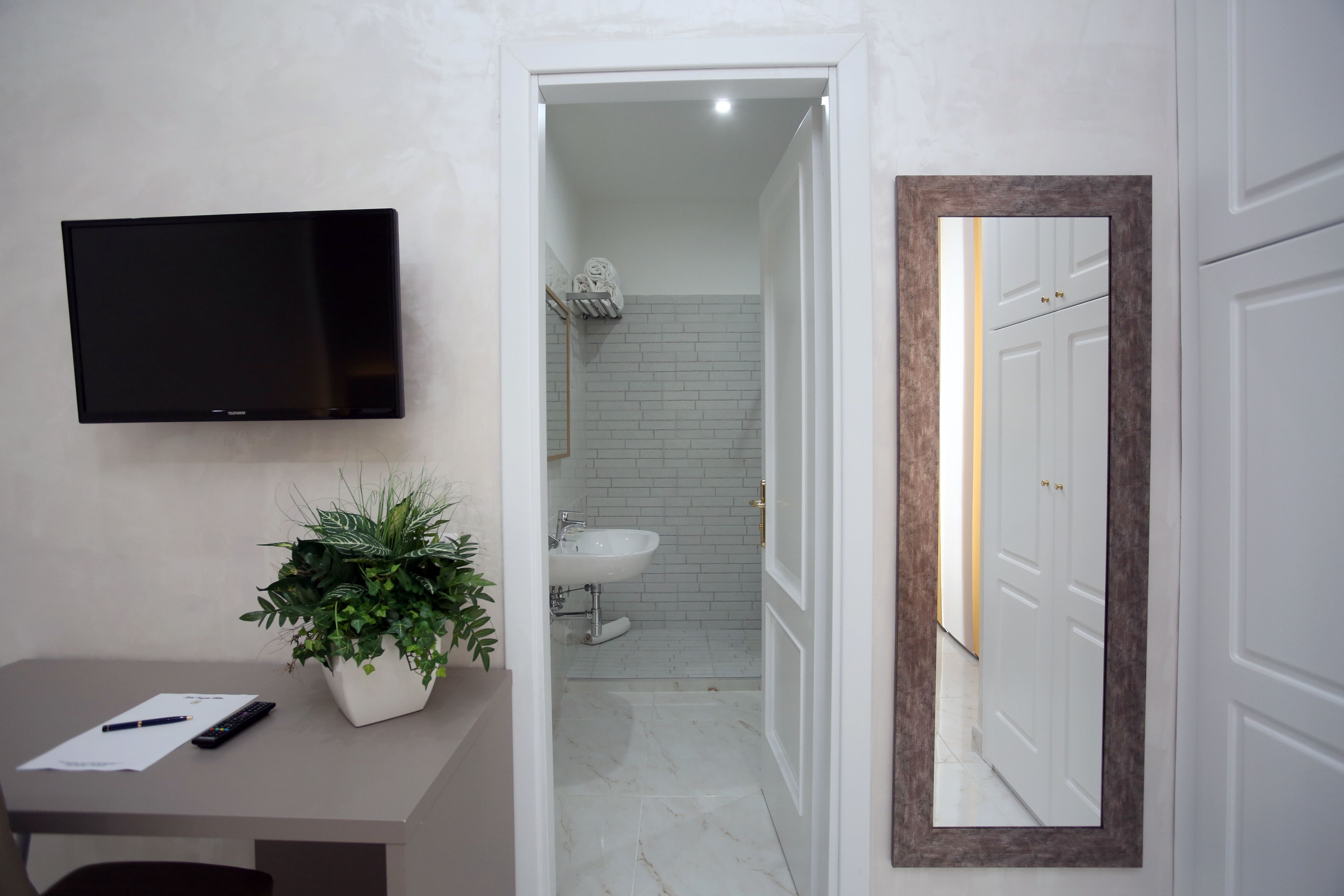 A bathroom with a white sink, a mirror with a brown frame, and a television mounted on the wall.